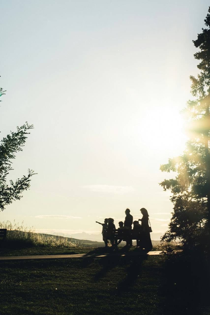A family gathered at a bench on a hilltop, silhouetted against a low evening sun