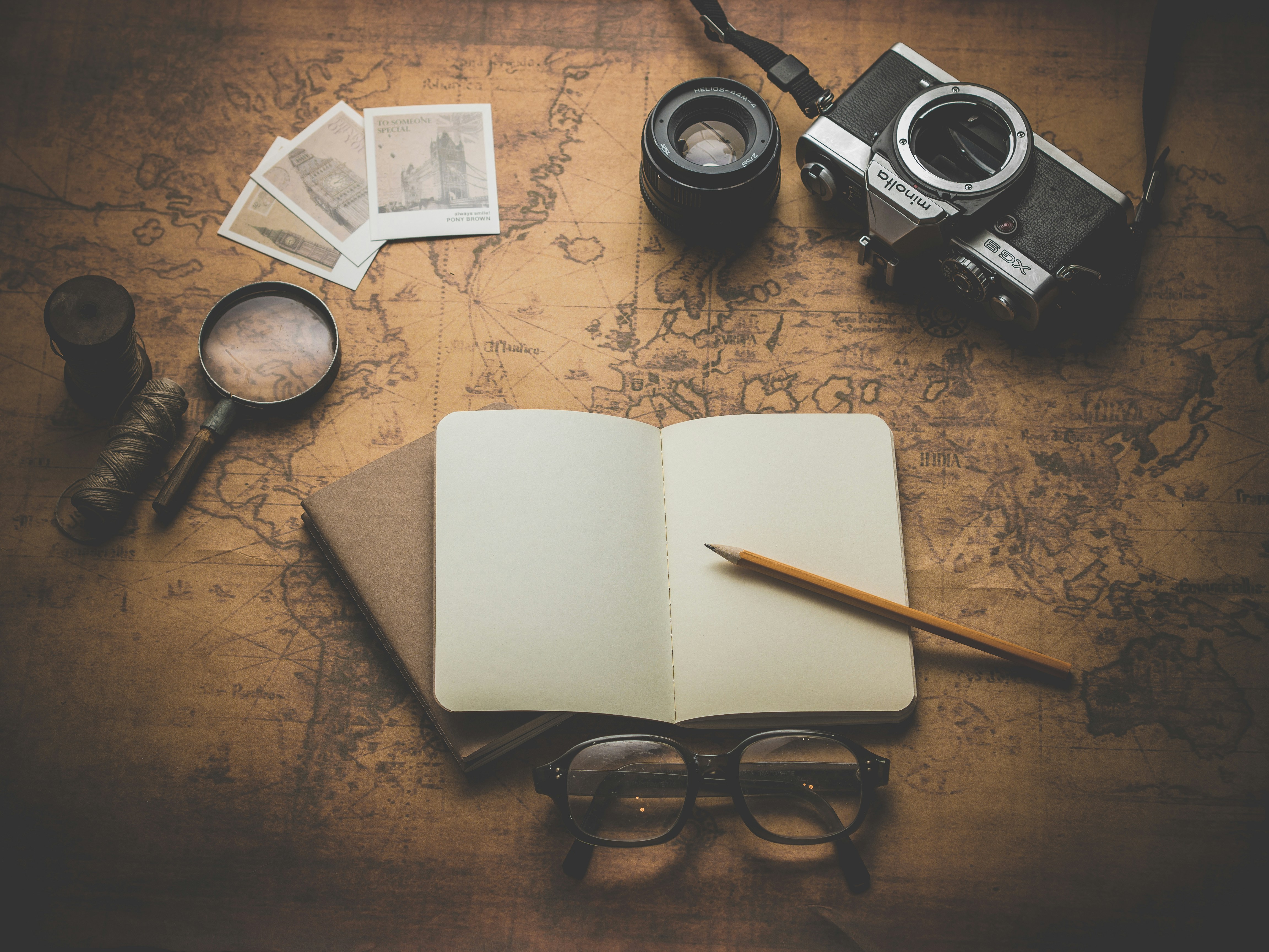 Open journal, camera, polaroids and magnifying glass on a vintage map