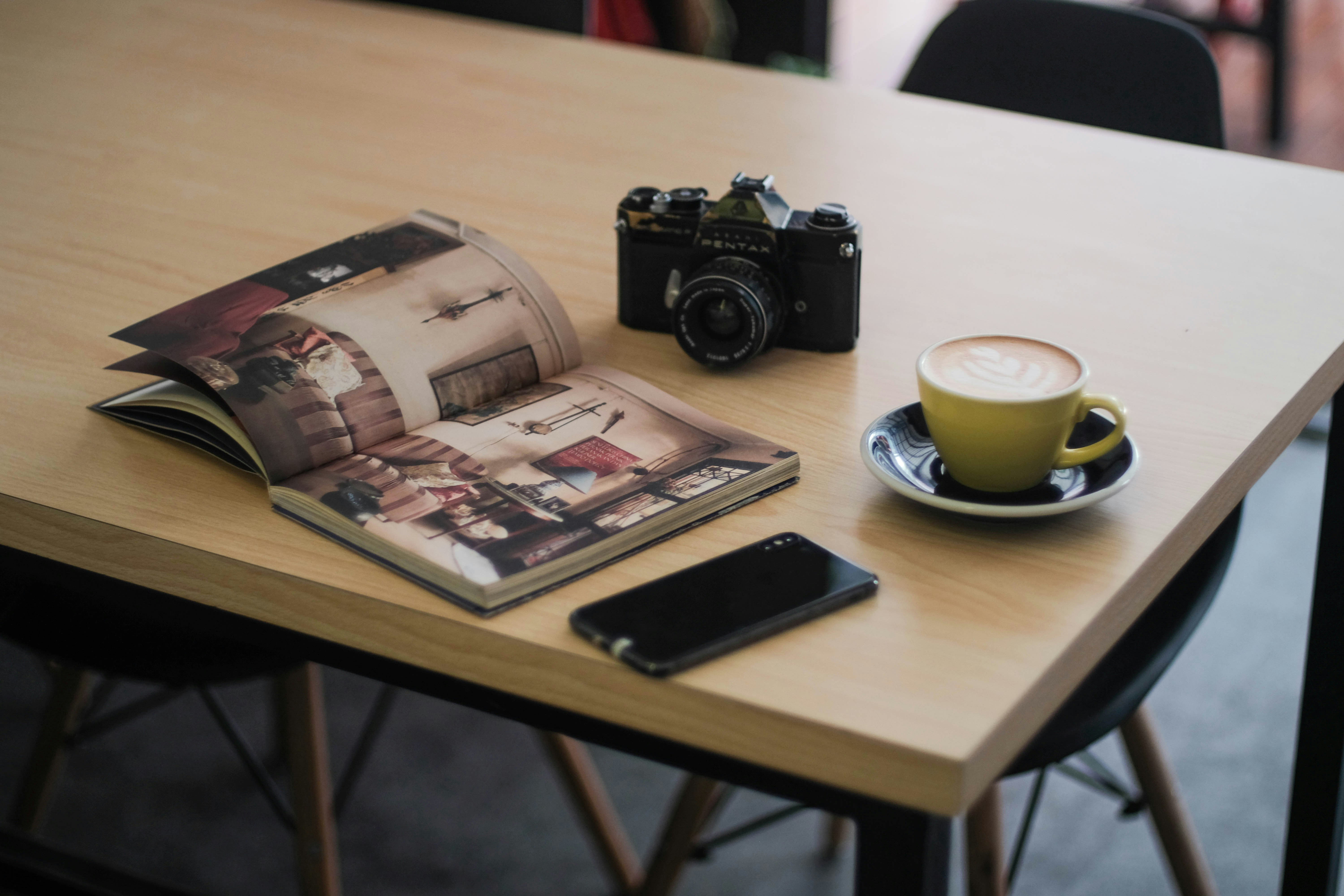 Open photo book on a table with a Pentax camera and a latte